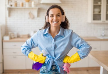 Gülümseyen Avrupalı bir kadının portresi rahat kıyafetler ve temizlik spreyi ve bez parçasıyla poz veren lastik eldivenler, mutfakta dikilen, evi çekip çeviren