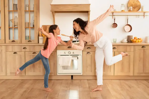 Happy European Mom And Daughter Kid Dancing And Singing With Spoons In Kitchen Interior. Full Length Shot Of Mother And Little Girl Fooling And Having Fun Together At Home