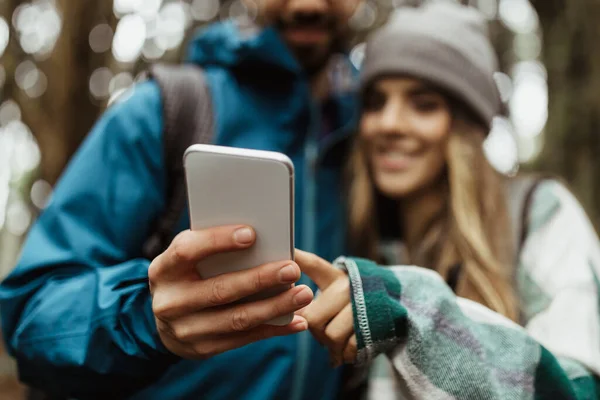 在智能手机上 一对穿着夹克的积极的高加索年轻夫妇计划着路线图 秋天在寒冷的森林里观看视频 被收割了 一起度假 积极的生活方式 冒险和旅行博客 — 图库照片