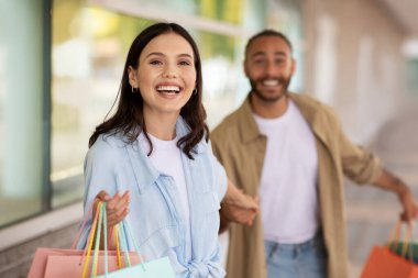 Kafkasyalı mutlu genç kadın kocasına bir sürü paketle yol gösteriyor, büyük indirimlerin, alışverişin ve yürüyüşün tadını çıkarıyor, dışarıda. Alışverişkolik duygular, satın alma, tavsiye satışı, reklam ve teklif