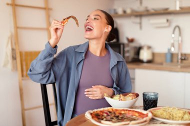 Hamilelik boyunca yiyecekler lezzetlidir. Bekleyen genç bayan pizza yemekten, makarna ve salatayla masaya oturmaktan, sıcak mutfak içlerinden, boş alanlardan hoşlanır.