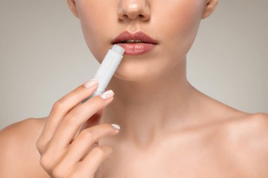 Mükemmel cilde sahip ciddi bir Avrupalı kadın ruj sürüyor, rutin prosedürlerden zevk alıyor, gri stüdyo arka planında izole edilmiş. Nemlendirici, temel çıplak makyaj, güzellik, cilt bakımı