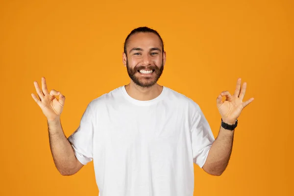 微笑的欧洲裔成年人的胡子在白色的T恤制作确定的签名手 孤立在橙色工作室背景 销售和生活方式 人类情感 广告和提供 — 图库照片