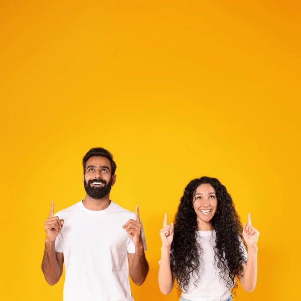 これをチェック 黄色いスタジオの背景の上に両手で指を指して幸せなアラビアのカップルのスクエアショット 若い配偶者は頭の上に空白のスペースを示しています 素晴らしいオファー — ストック写真