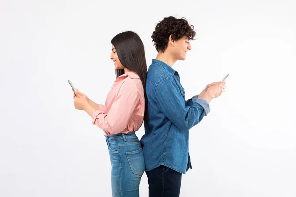 Gadżety Związki Wesoła Młoda Para Patrząca Telefony Stojące Tyłem Białym — Zdjęcie stockowe