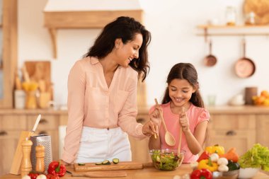Avrupalı anne ve küçük kızı evde sağlıklı organik sebzelerle taze salata hazırlarken akşam yemeği hazırlıyorlardı, mutfak masasının yanında poz veriyorlardı. Beslenme, Gıda Tarifleri