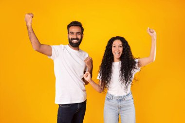 Zafer Kutlaması. Mutlu Ortadoğu Eşleri Neşeli İfadeyle Yumruk Sallıyor, Kollarını Kaldırıyor ve Stüdyoda Sarı Arkaplanda Kamera Pozisyonuna Gülümsüyor. Genel Başarı, Başarı