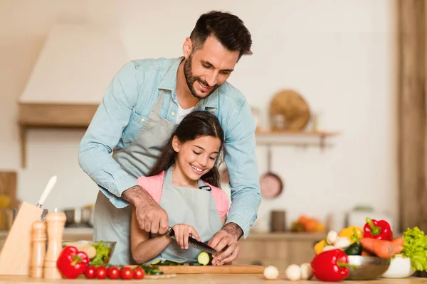 Cooking with dad. Happy girl preparing dinner with her father in kitchen, loving daddy making vegetable salad with his preteen child girl, free space