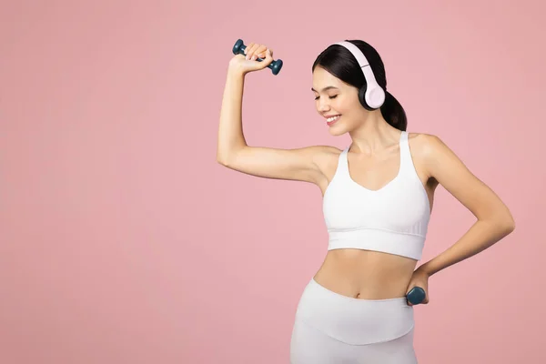 Pozitivní Evropanka Sportovním Oblečení Bezdrátových Sluchátkách Cvičí Činkami Pózuje Růžovém — Stock fotografie