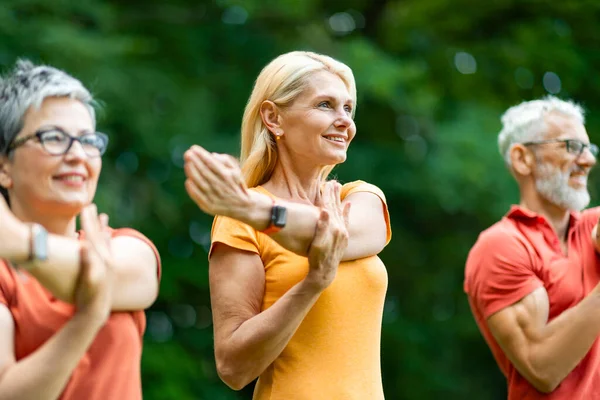 Group Of Happy Senior People Training Outdoors, Smiling Older Men And Women Stretching Arm Muscles While Standing Outside In Green Park, Sporty Mature Friends Enjoying Healthy Lifestyle, Closeup