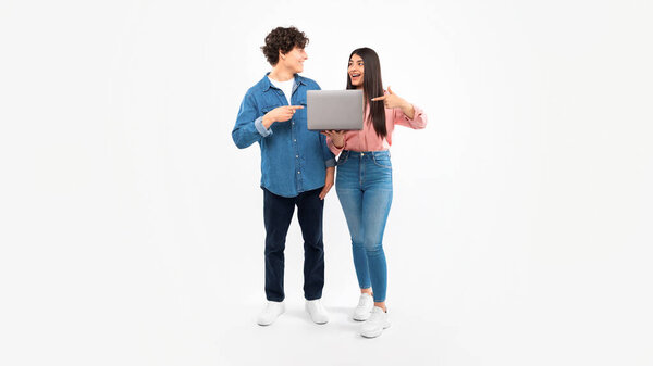 Online Offer. Students Young Couple Holding Laptop Together And Pointing Fingers At Computer Gadget, Recommending Website For E-Learning Over White Studio Background. Panorama