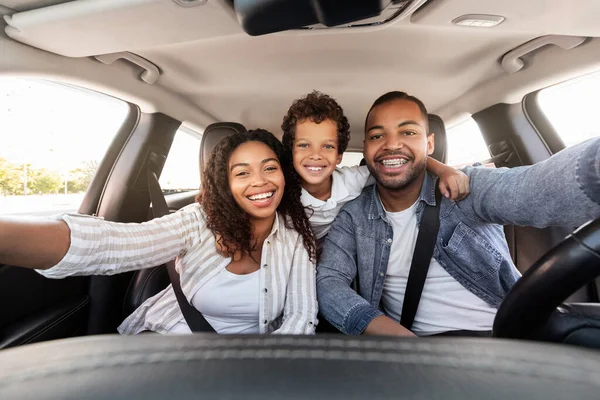 Cheerful african american family taking selfie while travelling together by automobile, smiling at camera on auto dashboard. Positive cool preteen black boy embracing father and mother, have car ride