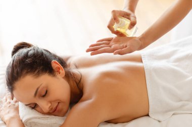 Rahatlatıcı masaj. Masör cildine vücut yağı sürerken ve güzellik salonunda rahatlamak için masaj yaparken, gözleri kapalı yatan bayan, kapanış. Şımartma ve Rahatlama