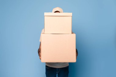 Tanımlanamayan kurye elinde bir sürü büyük karton kutu, paket teslimatı, mavi arka planda poz verme, maket, tasarım için yer