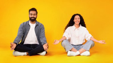 Birlikte meditasyon. Gülümseyen Arap Genç Çift, Lotus Poz Vererek Meditasyon Yapıyor, Sarı Stüdyo Arkaplanı Üzerinde Gözler Kapalıyken Rahatlamanın keyfini çıkarıyor. Yoga egzersizi yapıyorum. Panorama
