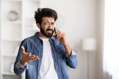 Evde cep telefonuyla konuşan stresli Hintli genç bir adamın portresi evde dikilen ve rahatsız edici telefon konuşmaları, acı çeken sorunlar, kopyalama alanı.