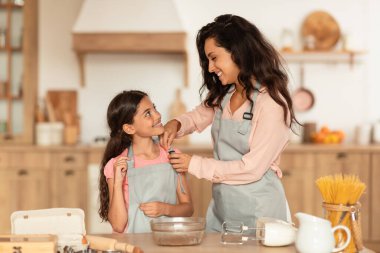 Birlikte yemek pişirmek. Mutlu anne, kızları önlükle mutfakta kurabiye pişirmeye hazırlanıyor, yemek masasının yanında duruyor ve hafta sonları evde lezzetli hamur işleri yapıyor. Aile Beslenmesi