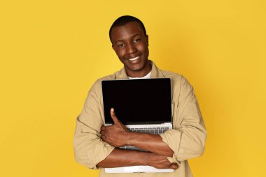 Bin yıllık neşeli Afro-Amerikan adam. Sıradan bir kucak dolusu dizüstü bilgisayar, izole edilmiş sarı bir stüdyo geçmişi var. Reklam ve teklif, teknoloji aşkı, çalışma ve uzaktan eğitim aracı