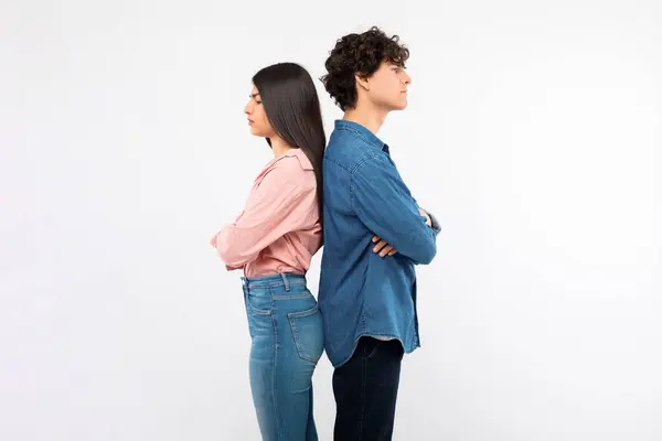 Offence. Frustrated young couple standing back to back sulking and not talking, posing on white studio background, crossing arms. Side view of girlfriend and boyfriend having issue in relationship