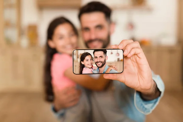 Bonding concept. Closeup portrait of happy father taking selfie with his daughter on cellphone, closeup. Smiling dad and girl making picture, selective focus on device screen, blurred background
