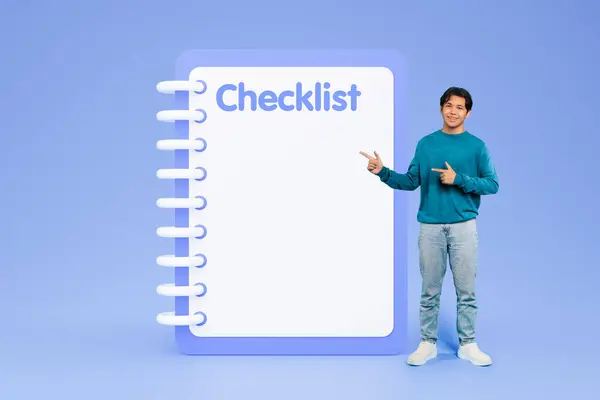 Cheerful young korean man in casual points fingers at big checklist with free space, isolated on blue studio background. Time management recommendation, day planning, business, study, motivation