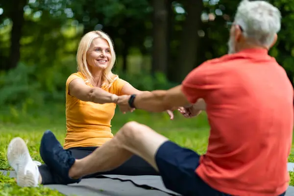 Happy Senior Couple Stretching Arms While Training Together Outdoors, Smiling Mature Spouses Exercising In Park, Sitting On Fitness Mats, Active Older Man And Woman Enjoying Healthy Lifestyle