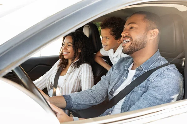 Cheerful African American millennial parents enjoying great weekend with their school aged kid, riding white car, looking at road and smiling. Happy mother, father and son sitting inside auto