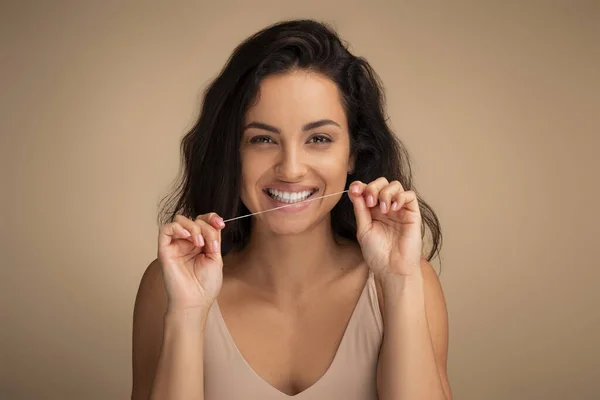 Portrait of happy attractive millennial toothy brunette lady model flossing mouth for clean oral hygiene. Indian woman cleaning teeth with dental floss, isolated on studio background, closeup