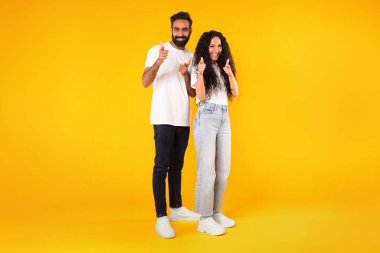 Sırada sen varsın. Mutlu genç Arap erkek ve kadın, sarı stüdyo arka planındaki kameraya bakıp seni tavsiye ediyor ve seçiyor. Çiftin tam boy çekimi, boş alan