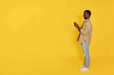 Bin yıllık neşeli Afro-Amerikan adam telefonda sohbet ediyor, sarı stüdyo geçmişinde soyutlanmış, tam boy, profil. Reklam ve teklif, uzaktan iletişim uygulaması, sosyal ağlar, blog