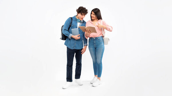 Academic Achievement. Cheerful Student Lady Showing her Workbook To Boyfriend, Bragging About Great Grades, Standing With Workbooks And Backpacks Over White Studio Background, Panorama