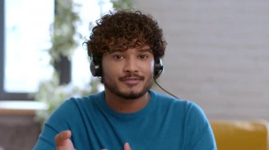 Yardım hattı servisi. Webcam pov portresi genç Hintli adam müşteri destek yöneticisi kulaklık takıyor video sohbet yoluyla müşteriyle konuşuyor, sorunu nasıl çözeceğini anlatıyor, ev ofisinde çalışıyor