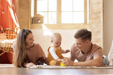 Üç kişilik mutlu bir aile, bebekler evde birlikte vakit geçiriyorlar, oturma odasında oyuncaklar oynuyorlar, gülümseyen genç bir anne ve baba sevimli bir çocukla bağ kuruyor, boş alan yaratıyorlar.