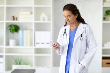 Neşeli, olgun, çekici esmer kadın. Tıp üniformalı doktor. Klinikte akıllı telefon kullanıyor, hastayla sohbet ediyor. Doktorunla irtibatta kal.