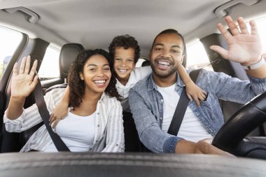 Arabayla seyahat ederken fotoğraf çeken sevimli, mutlu siyah aile. Otomatik gösterge panelinde kameraya el sallıyorlar. Olumlu afro-amerikan çocuk anne ve babayı kucaklıyor, kameraya gülümsüyor