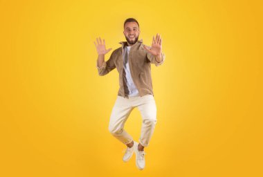 Gündelik sakallı neşeli beyaz adam eğleniyor, zıplıyor, havada donuyor, sarı stüdyo arka planında izole edilmiş. Zafer, satış, yaşam tarzı ve insani duygular.