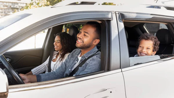 Happy friendly black family riding car traveling by automobile. African American parents and school aged son enjoying road trip together on weekend. Family leisure, affectionate, love, relationships