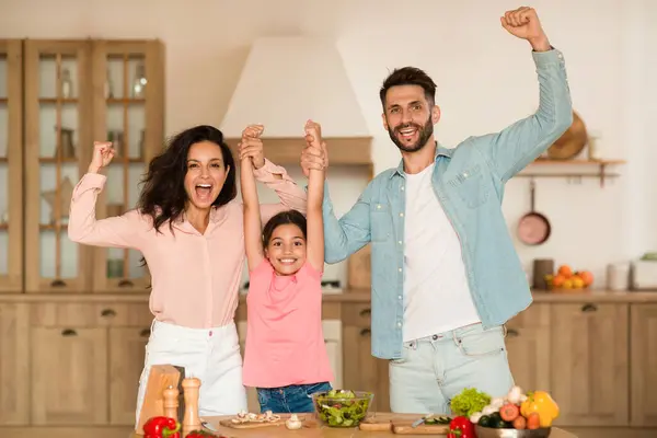 欢乐的家人牵着手 挥动拳头 在厨房里一起准备晚餐时表示是的 家长和女孩在做饭时很开心 — 图库照片