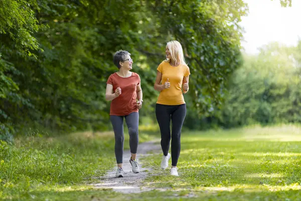 Two Sporty Senior Woman Jogging Together In Park, Happy Older Ladies Running Outdoors, Mature Friends Training Outside, Enjoying Active Lifestyle, Full Length Shot With Copy Space