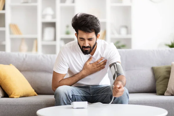 Health Problems Concept. Young Indian Man Feeling Heart Pain At Home, Checking Blood Pressure With Upper Arm Monitor And Rubbing Chest, Sick Eastern Man Measuring Arterial Tension, Free Space
