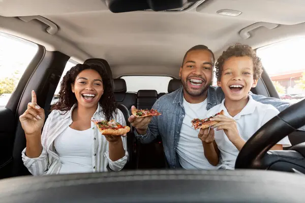 Cheerful african american family sitting in car, eat delicious pizza. Loving black father, mother and preteen child boy son have road trip on weekend, have snack while travelling, enjoy time together