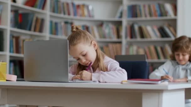 学费概念 集中注意力的小女孩坐在课桌前 在课上看笔记本电脑 在笔记本上写字 跟踪镜头 慢动作 自由自在的景象 — 图库视频影像