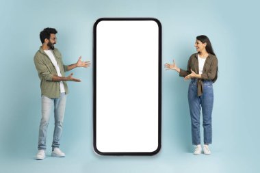 Alışveriş mobil uygulaması, Kara Cuma teklifi, sezon indirimi. Beyaz ekran, mavi stüdyo arka planı, maketi, fotokopi alanı, tam uzunlukta olan büyük telefonlu mutlu Hintli kadın ve erkek.