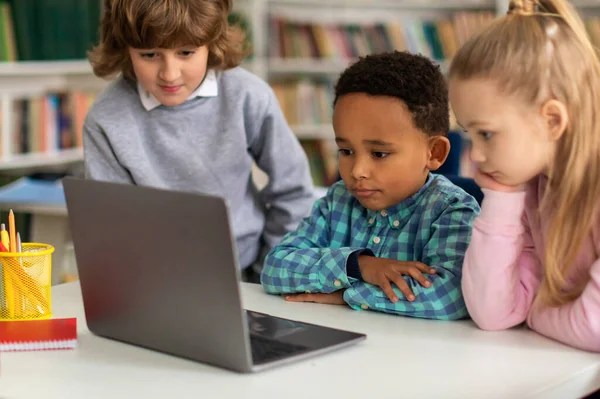 stock image Diverse group of three enthusiastic school children engaged in educational activities, attentively exploring and learning together via laptop in primary school classroom