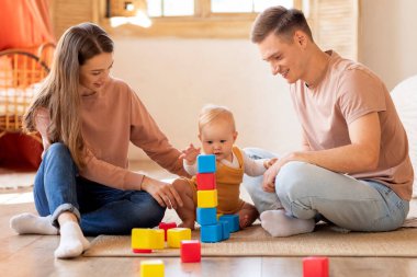 Mutlu, genç, beyaz bir aile evde bebekleriyle blok inşa ediyor neşeli bir ebeveyn ve sevimli bir çocuk oturma odasında otururken oyuncaklarla eğleniyor.
