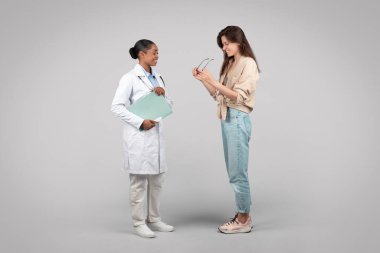 Mutlu siyahi kadın doktor, göz doktoru, yeni gözlük seçmede uzman hasta asistanı, gri arka plan stüdyosunda izole edilmiş. Vizyon iyileştirme, sağlık hizmetleri