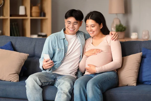 Happy Asian Man Pregnant Woman Using Smartphone Application Couch Home — Stock Photo, Image