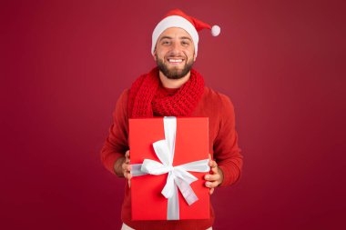 Gülümseyen yakışıklı beyaz adam, Noel Baba şapkalı sakallı, Noel hediyeli, yeni yıl tatilinin tadını çıkaran, Burgundy stüdyosunda izole edilmiş. Xmas 'ta mevcut yaşam tarzı