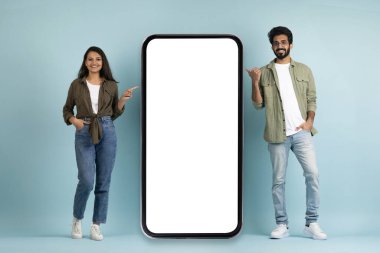 Sıradan güzel bir kadın ve beyaz ekranlı büyük cep telefonunu gösteren yakışıklı bir adam. Randevu uygulaması için bir model. Güzel teklif, mavi arka plan, tam boy.