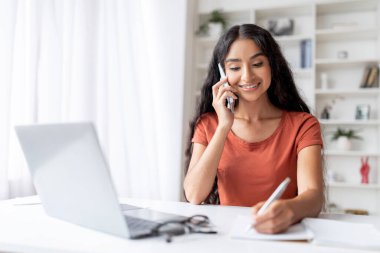Ofisteki verimli genç Hindu kadın işleri. Odaklanmış kadın işini sorunsuzca yürütüyor, önemli bir telefon görüşmesi ile dizüstü bilgisayar arasında geçiş yapıyor, evden işe yarayan çalışmalar sergiliyor.
